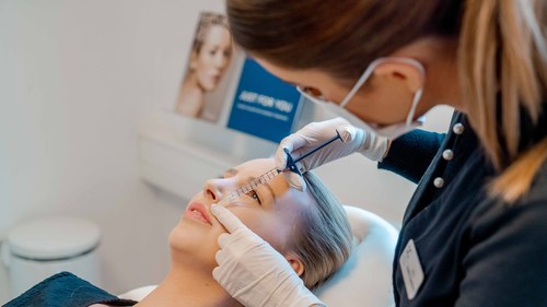 Behandler udfører ansigtsbehandling med injektionssprøjte